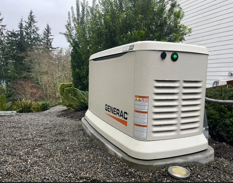 White Generac generator unit installed outdoors on gravel next to a house with landscaping and trees in the background