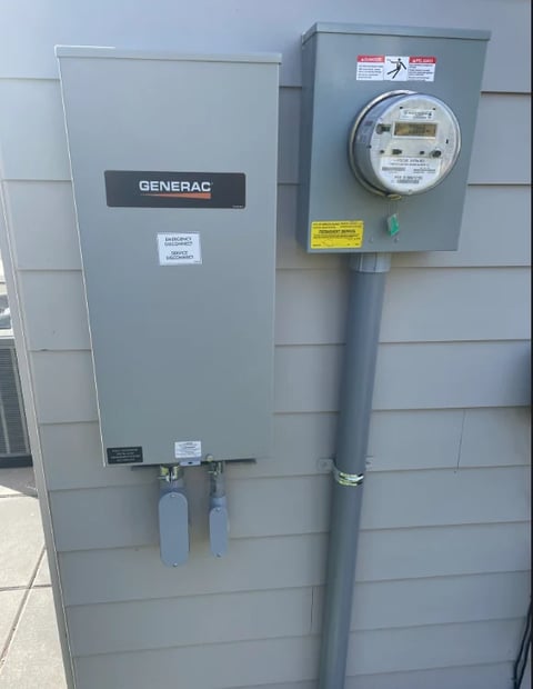 Generac transfer switch and utility meter mounted on exterior house wall with gray siding