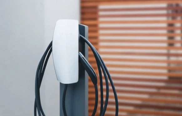 Electric vehicle charging cable with white connector and coiled black cords mounted on wall